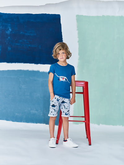 Jean Bourget short-sleeved T-shirt in cobalt blue cotton jersey is screen printed with a dinosaur skeleton carrying a surfboard.