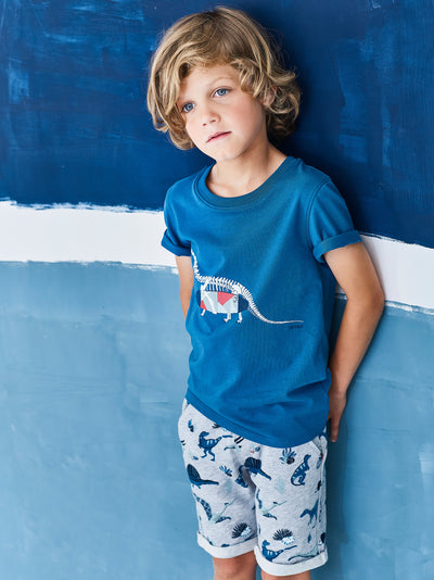 Jean Bourget short-sleeved T-shirt in cobalt blue cotton jersey is screen printed with a dinosaur skeleton carrying a surfboard.