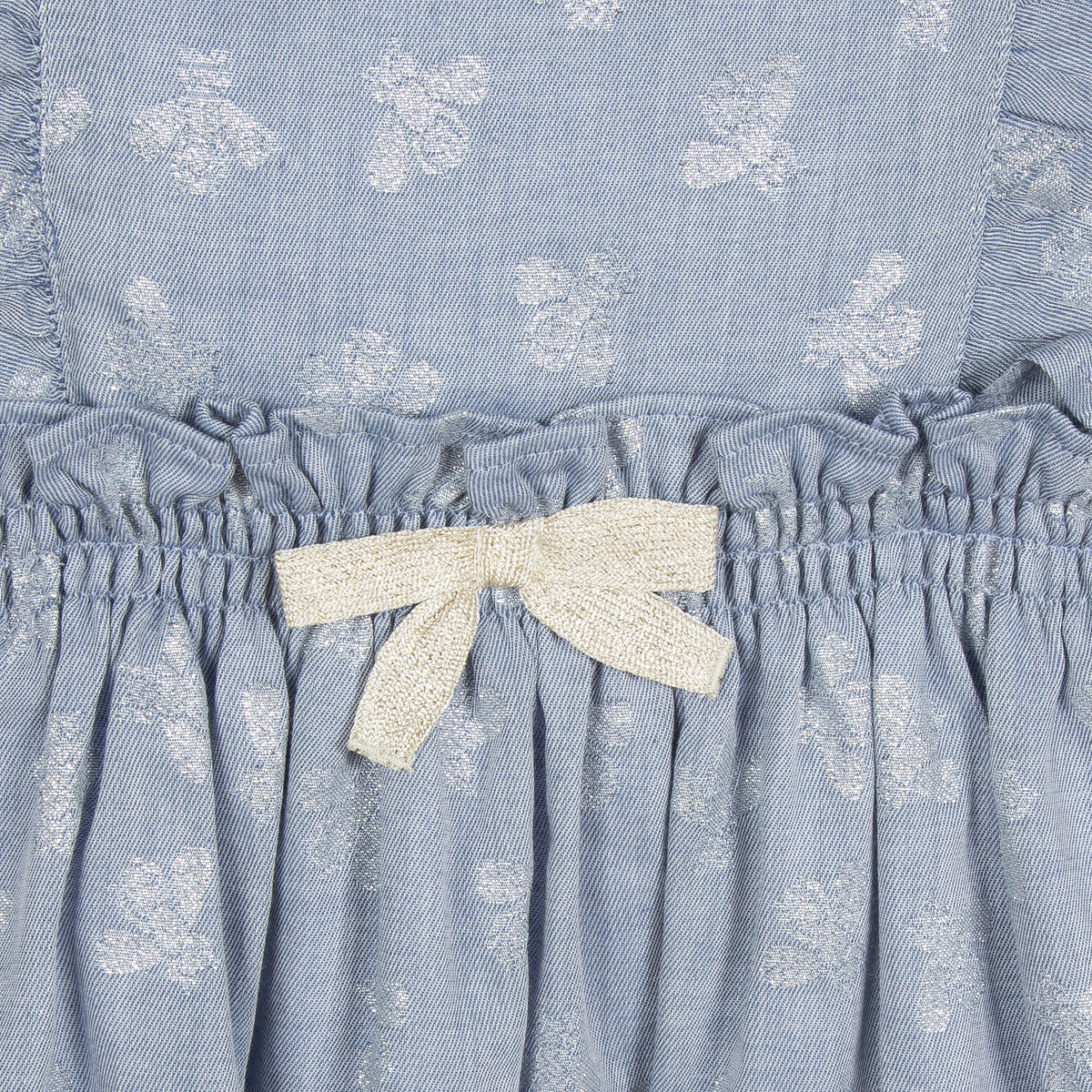 Jean Bourget light blue chambray dress is adorned with silver lurex bees in all over. The silhouette is animated with bands fluttering on the sides at the front and in the back. The skirt is pleated and the waist is bent by an elastic decorated with a golden bow.