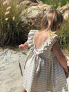 Backside of a little girl wearing a light grey dress with wide stripes and ruffles.